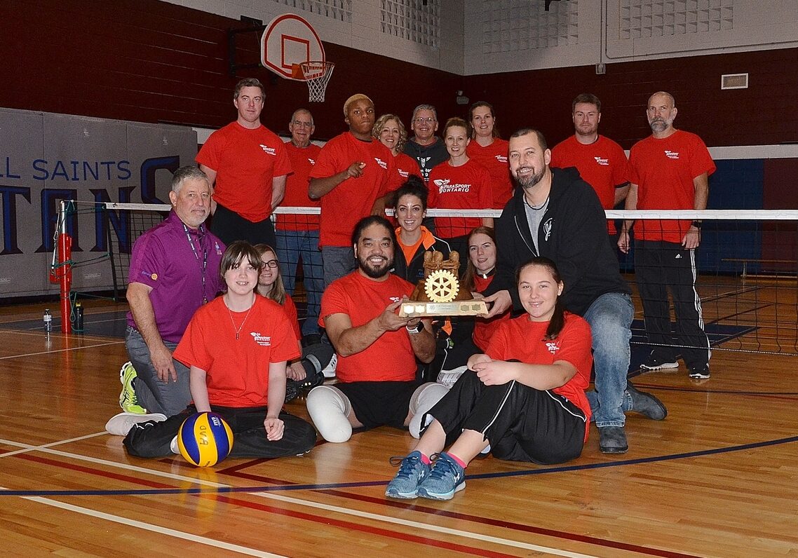 Para athletes in a group photo. Aristotle is holding a trophy on the foreground.